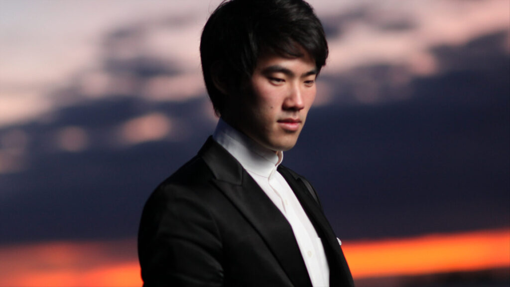 World-touring pianist Bruce Liu stands lit by a sunset sky. Press photo courtesy of the Boston Symphony Orchestra.