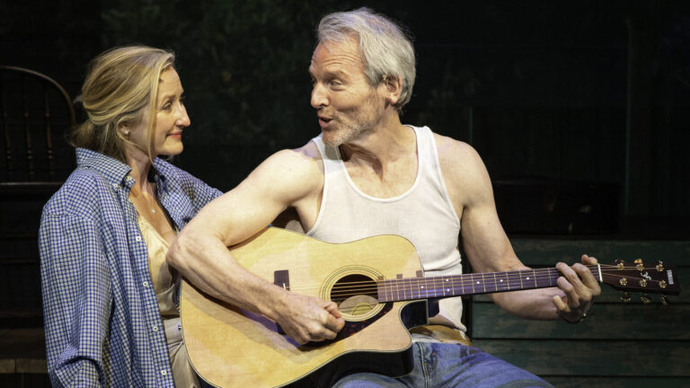 Lauren Ward and Stephen Bogardus laugh together as he strums a guitar in BTG’s production of On Cedar Street, 2023. Press photo courtesy of BTG