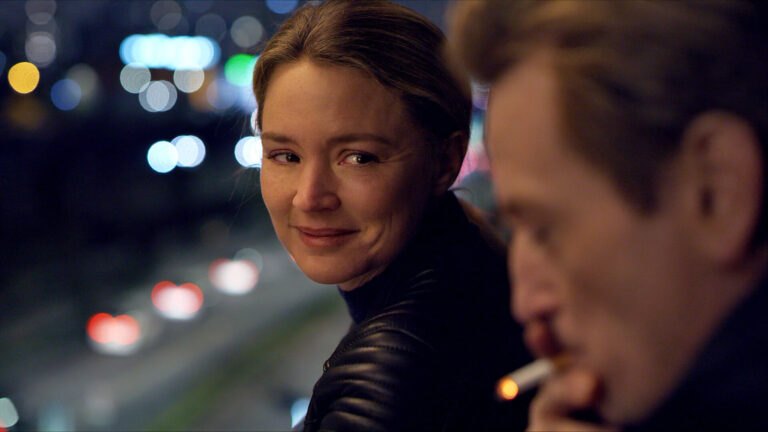 Mia (Virginie Efira) smiles at a companion on a city street at night in Revoir Paris. Press film still courtesy of Music Box Films
