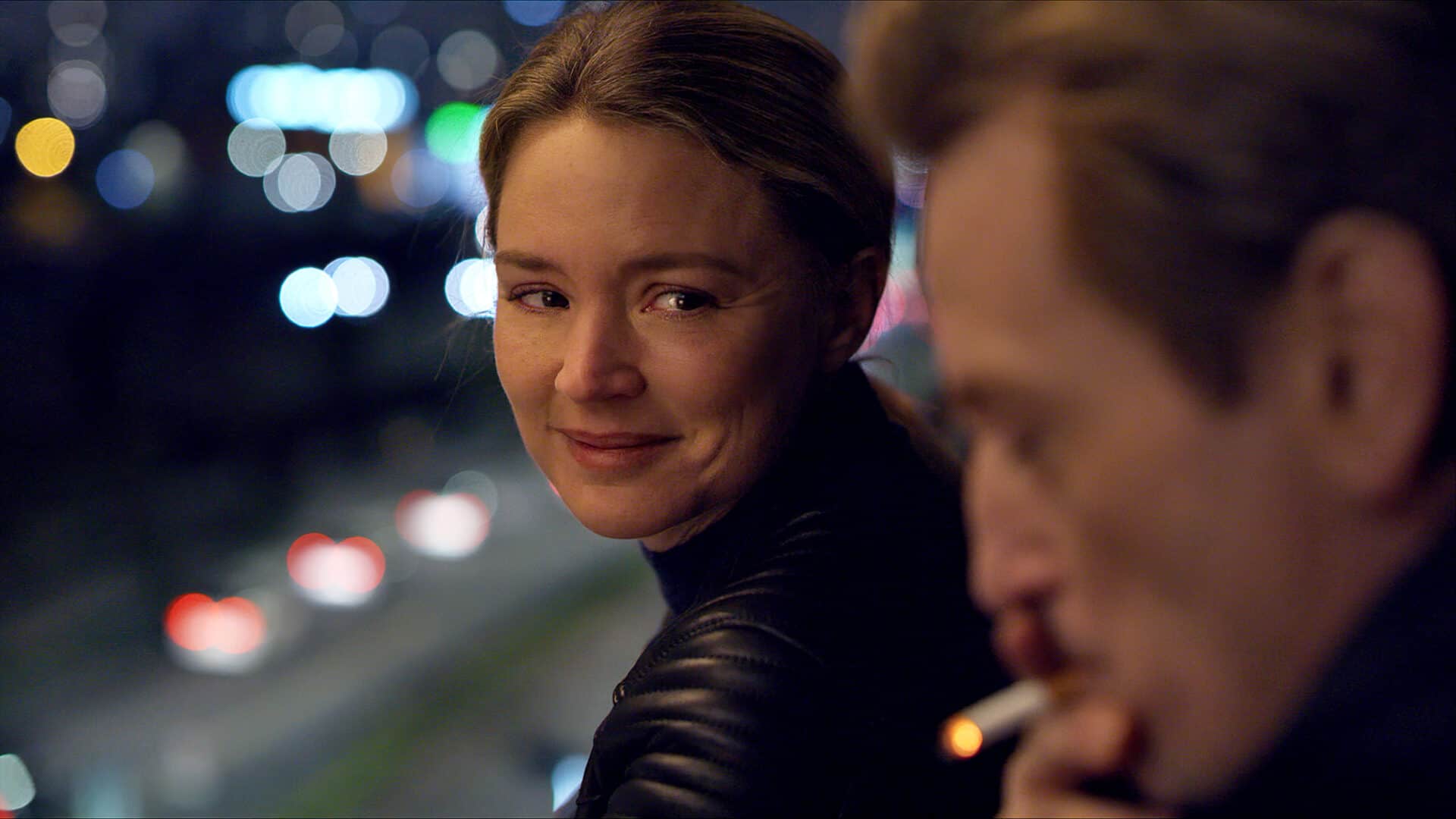 Mia (Virginie Efira) smiles at a companion on a city street at night in Revoir Paris. Press film still courtesy of Music Box Films