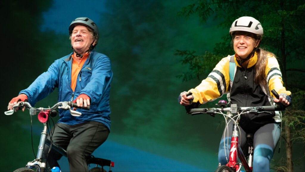 Bill Bowers as Terry and Esther Williamson as Mona ride bikes into the New Hampshire woods in Making of a Great Moment. Press photo courtesy of Chester Theatre Company