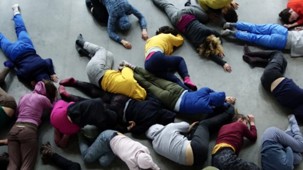 Performers in bright clothing lie curled on a grey floor, seen from above, in Clear Night by Kim Brandt, 2016. Press photo courtesy of the Clark Art Institute