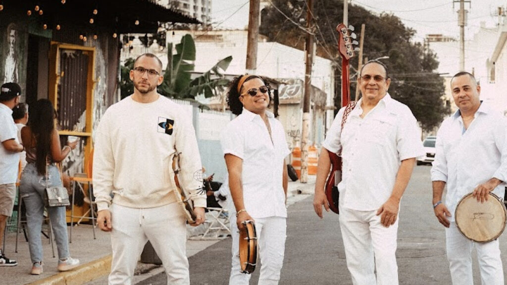 Multi-Grammy Award–nominated band Plena Libre, masters of the traditional Puerto Rican plena and bomba styles, walk down a city street in bright sun. Press photo courtesy of the artists