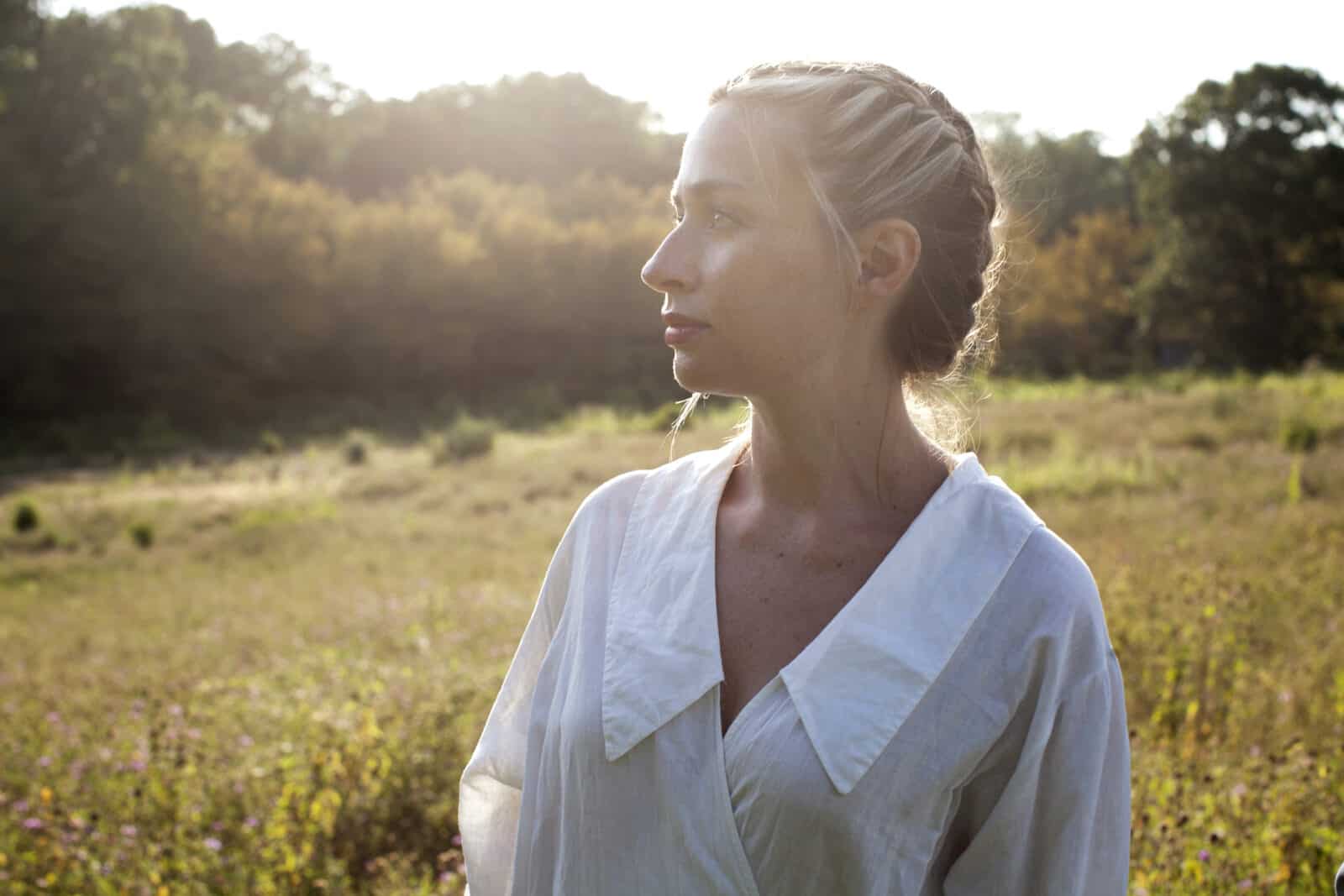 Internationally recognized composer Sarah Kirkland Snider stands in profile in a field in the sun. Press photo courtesy of the artist.