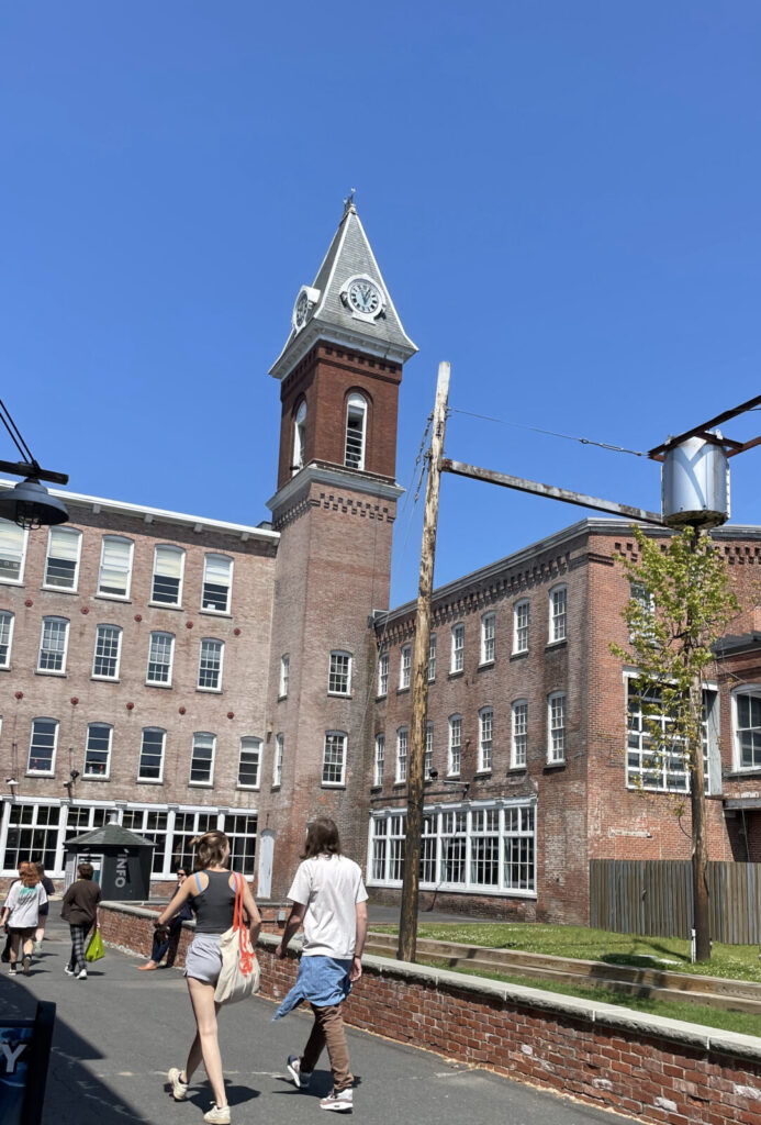 Visitors walk by the upside-down trees to the entrance to Mass MoCA on a vividly sunny day.