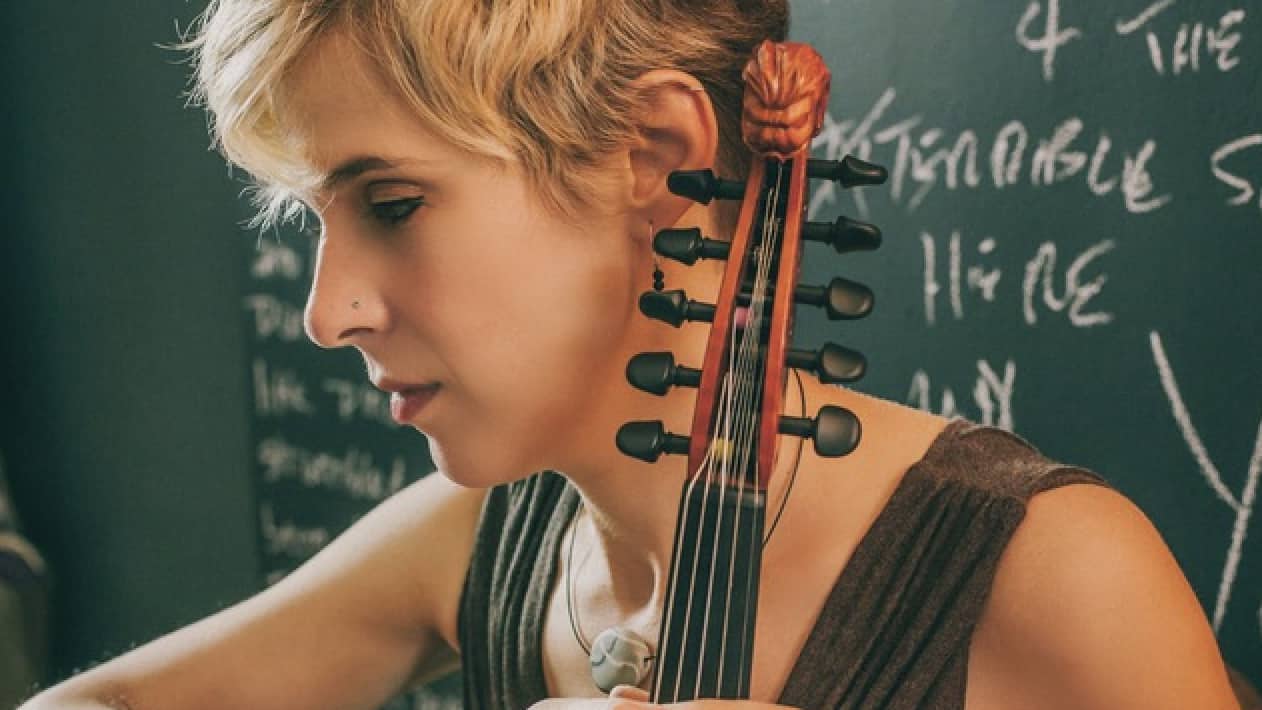 Grammy nominated jazz violinist Sara Caswell sits with her instrument against a green chalkboard. Press photo courtesy of Lulufest