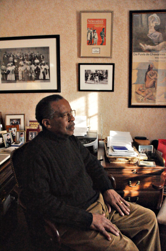 Skip Meade sits at a wooden desk in the sunlight surrounded by books and photographs.
