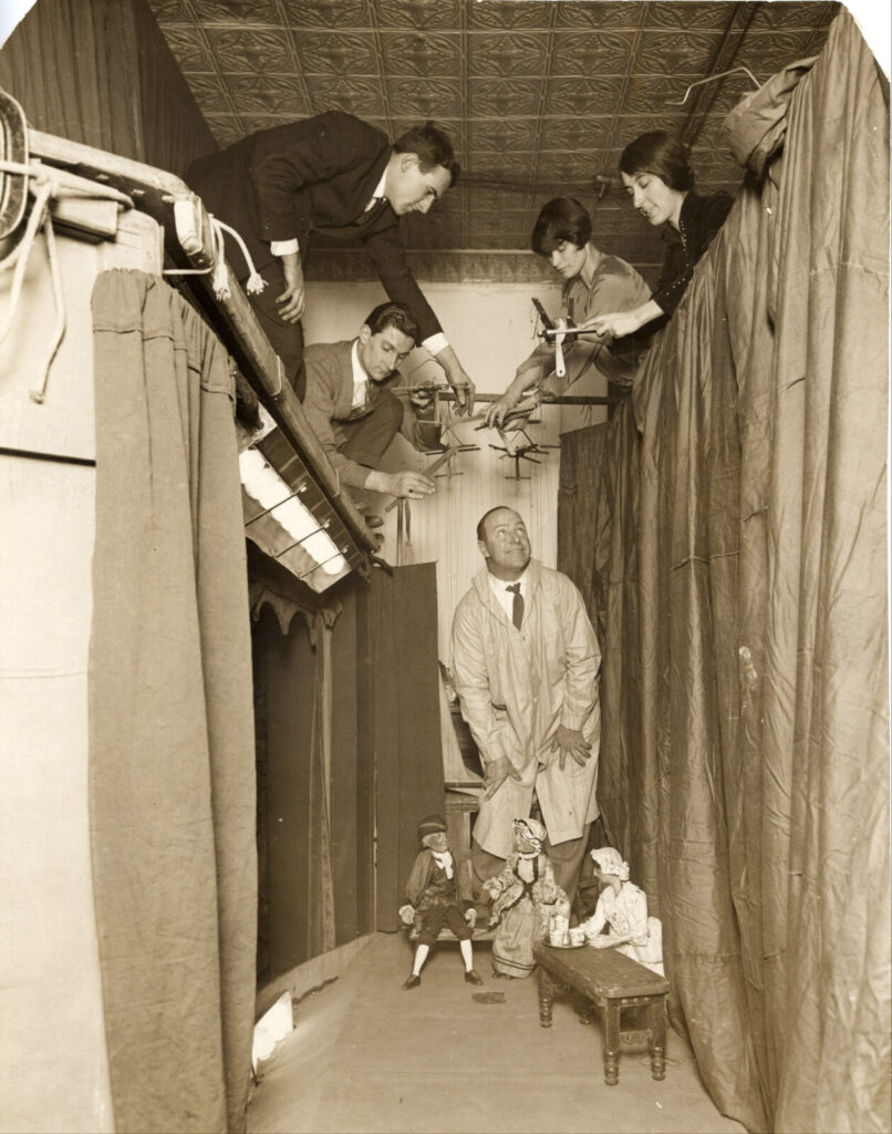 Tony Sarg walks into a puppet theater to talk with his troupe of puppeters in a black and white photograph. Press photo courtesy of the Norman Rockwell Museum