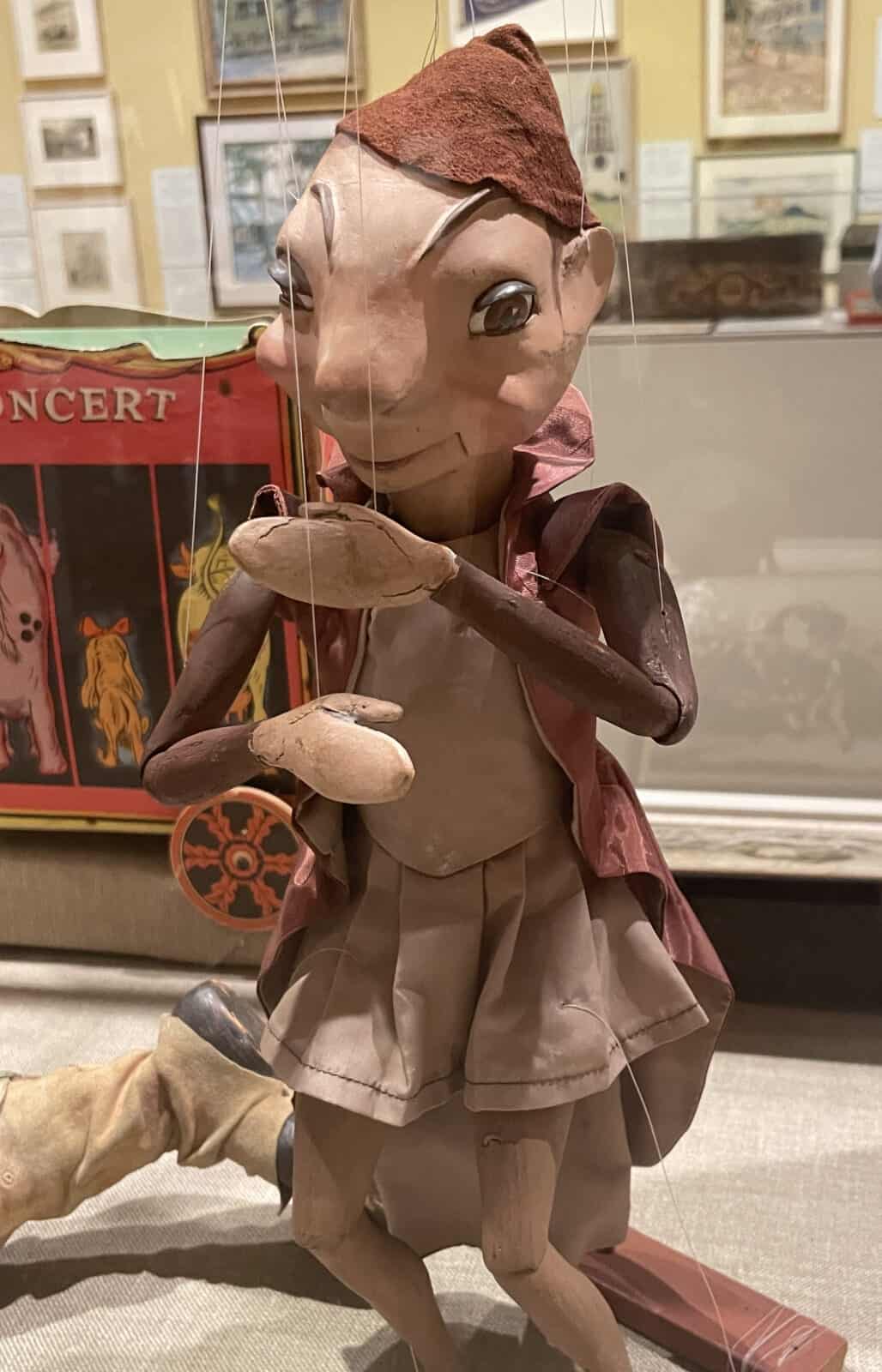 A puppet with eyebrows and ears suggestive of an elf or a firefly joins Tony Sarg's puppet theater cast of Pinocchio, with Sarg's artwork on the wall behind. Press photo by Kate Abbott, courtesy of the Norman Rockwell Museum