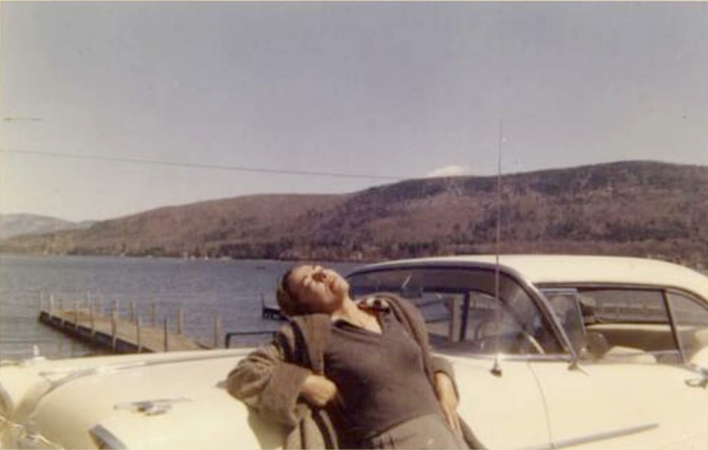 Yiddish fiction writer Blume Lempel rests against a white car in the sun by a lake in a historic photograph. Press photo courtesy of the Yiddish Book Center