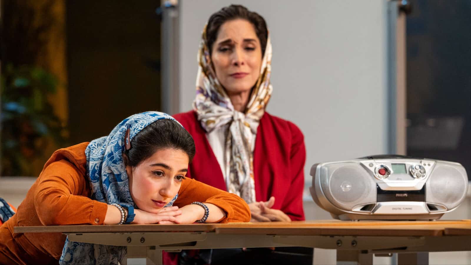 Pooya Mohseni as Roya looks on with kindness and humor as Narges Kalogli rests her chin on her hands and her head on a classroom table as Goli, a student in Iran, in Sanaz Toossi's play 'English' at Barrington stage. Press photo courtesy of BSC