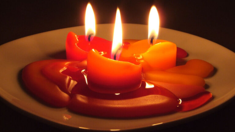 Three amber-colored candles burd together, melting down on a saucer. Creative Commons courtesy photo