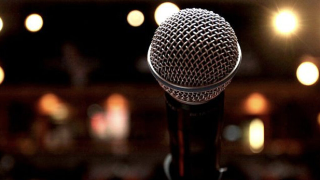 A microphone stands poised against a dark background gleaming with points of light. Creative Commons courtesy photo