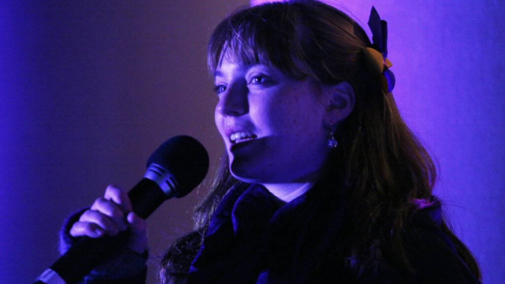A Williams student sings into a microphone indeep purple light at the Williams Teach It Forward celebration in 2015. Press photo courtesy of Williams College