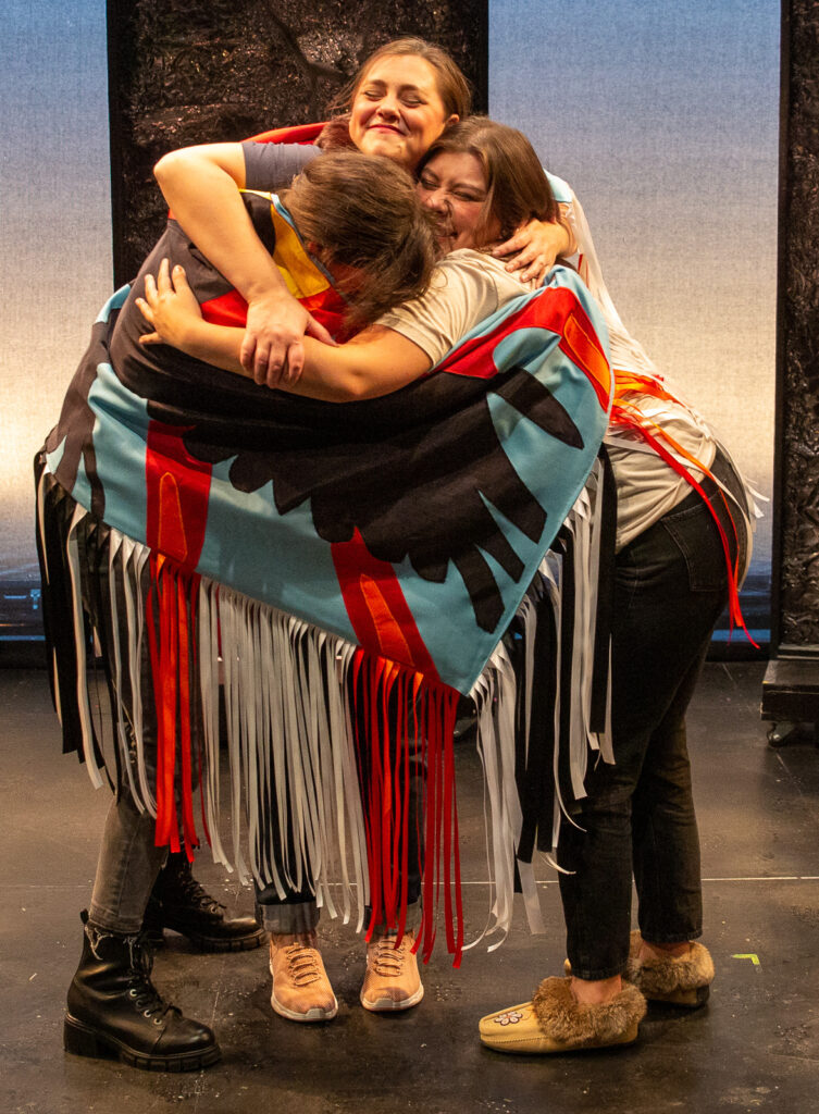 Ria Nez, Jasmine Rochelle Goodspeed, and Sarah B. Denison hold each other in the WAM Theatre production of KAMLOOPA by Kim Senklip Harvey, directed by Estefanía Fadul. Press photo courtesy of WAM Theatre