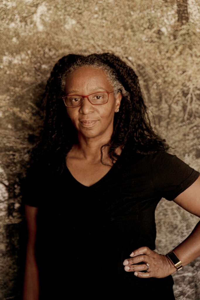 Photographer and artist Letitia Huckaby stands looking directly at the camera against and earthy background. Press image courtesy of WCMA and the artist