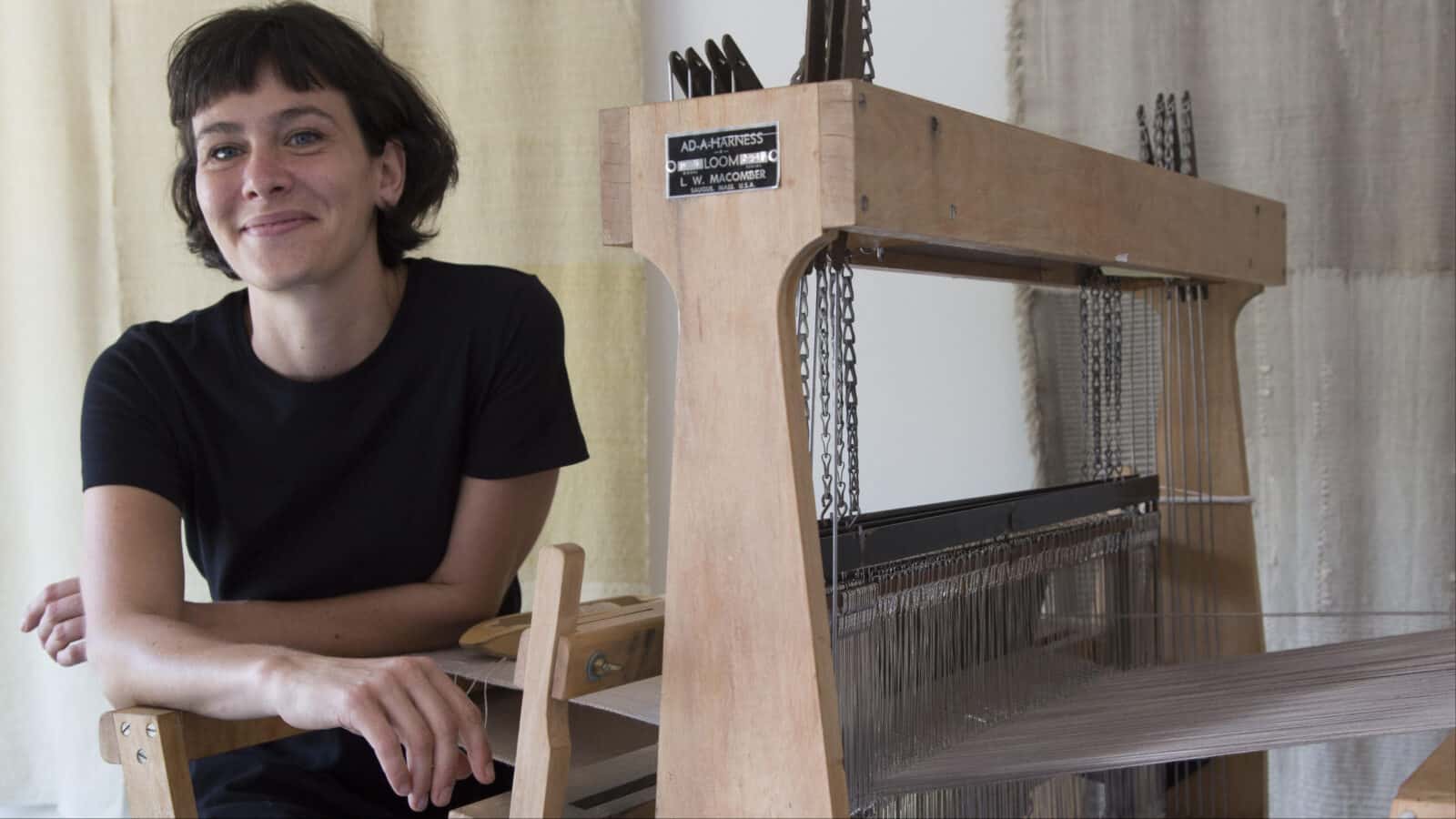 Fiber artist Jamie Goldenberg sits smiling by her loom. Press photo courtesy of Simon's Rock