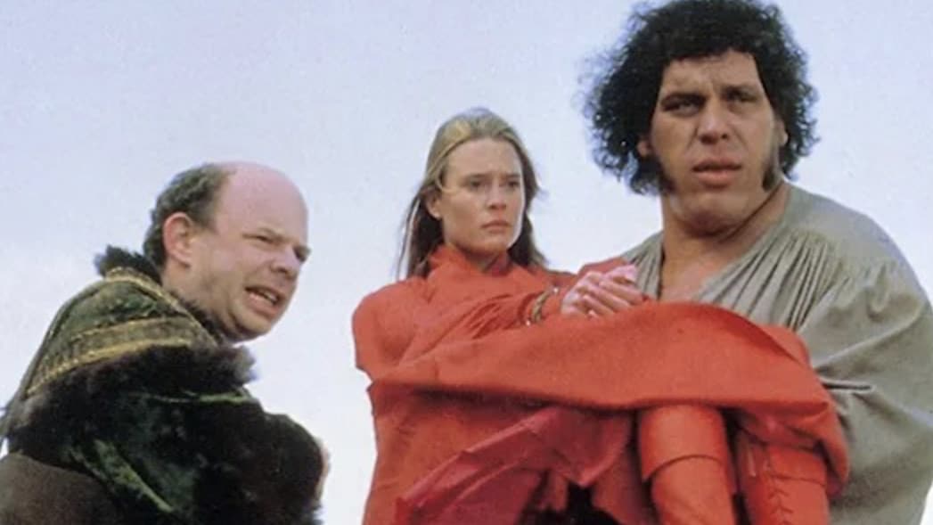 Wallace Shawn as Vizzini and Andre the Giant as Fezzik stand with open sky behind them and Robin Wright as Buttercup held in Fezzik's arms in the comedy adventure film the Princess Bride. Press photo courtesy of the Clark Art Institute