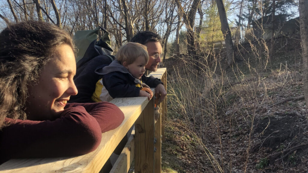 Kate Abbott and Markus and Corax Bergvind lean on a rail on the North Hoosic bike path as Yves Corbiere takes a photo in late afternoon sunlight.
